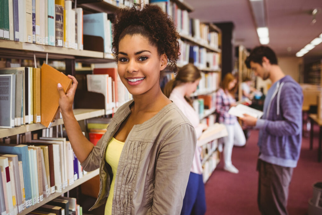 Smiling student picking out a book in library