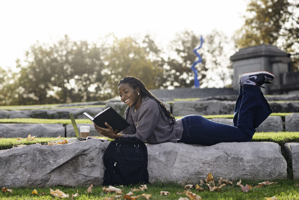 Student laying on her stomach reading a book outside.