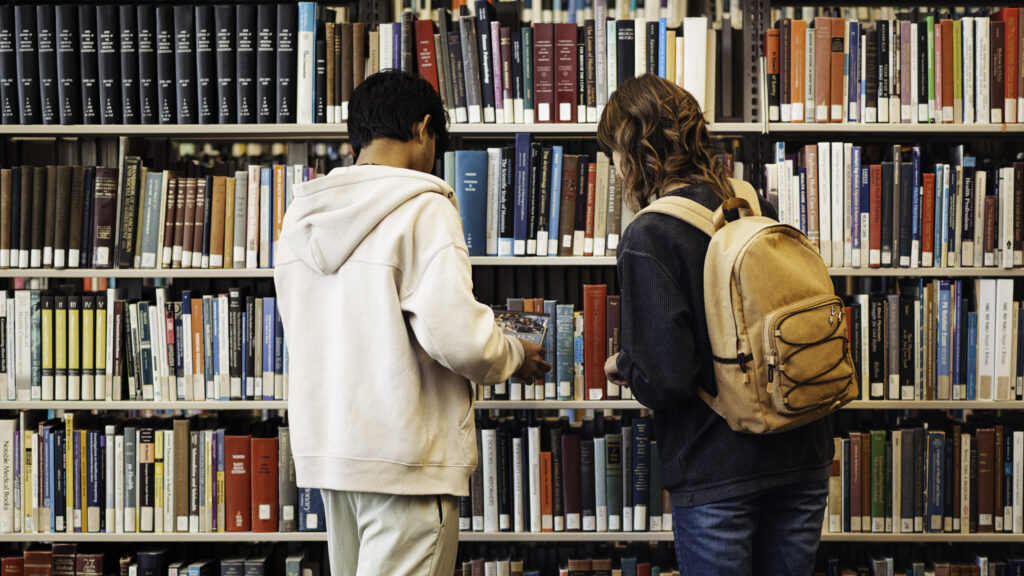 Two students in front of a bookcase.