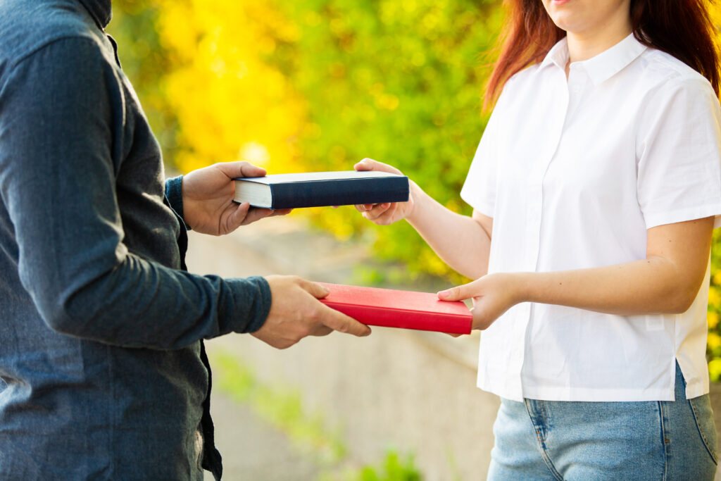 Two people handing from the shoulders down, trading books.