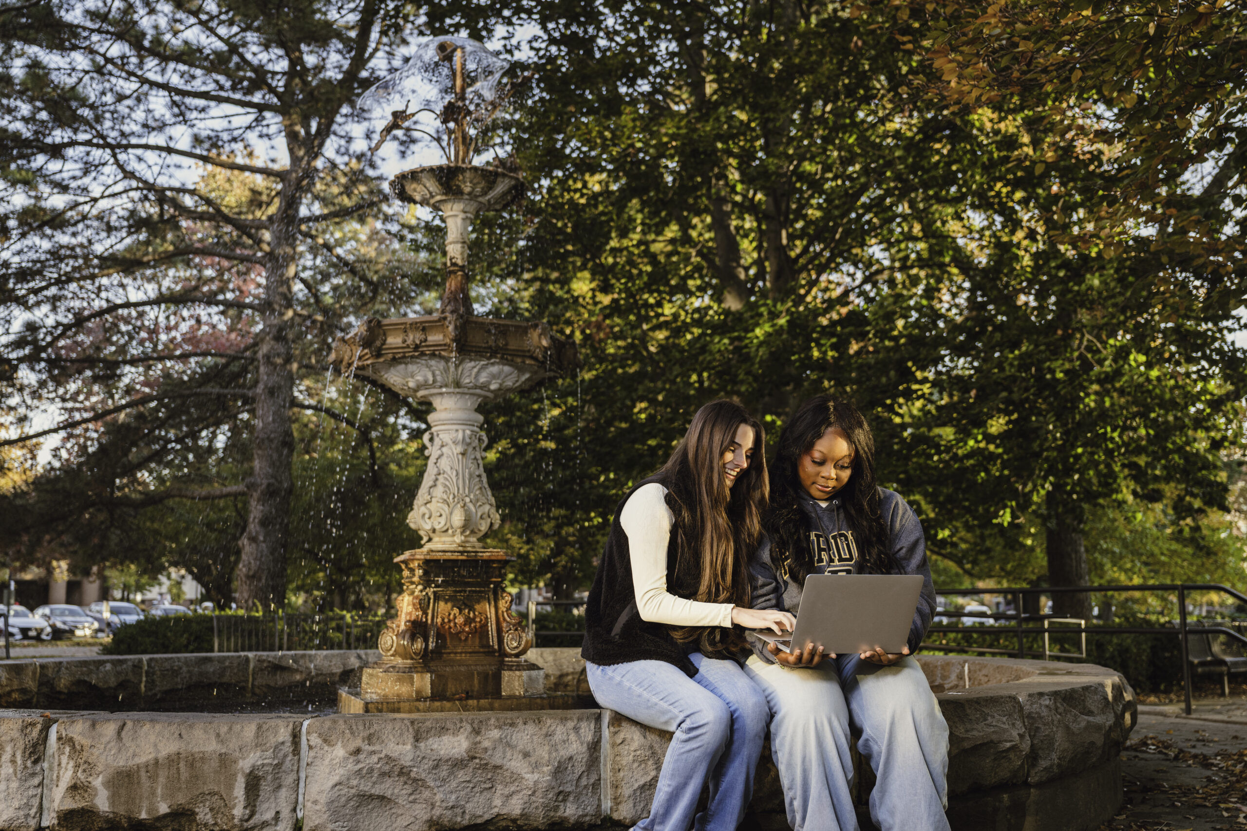 Two students sitting next to each other, looking at a computer.