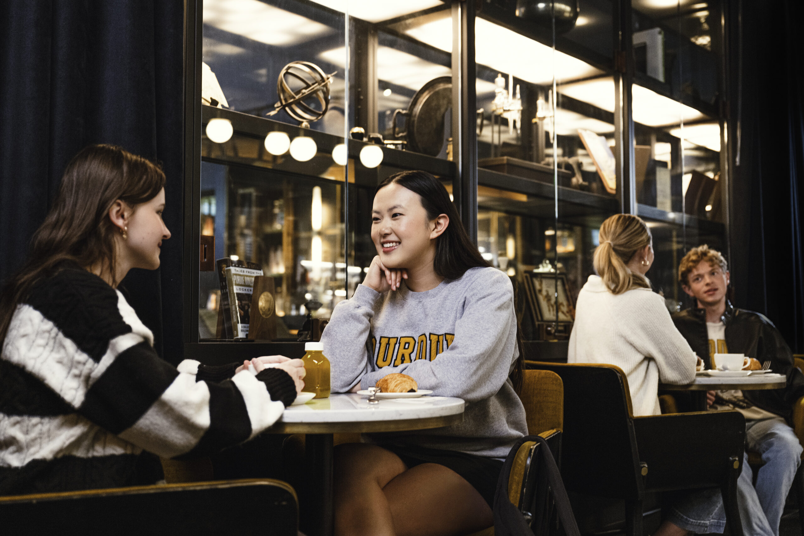 Two young women sit at a small table inside a cafe.